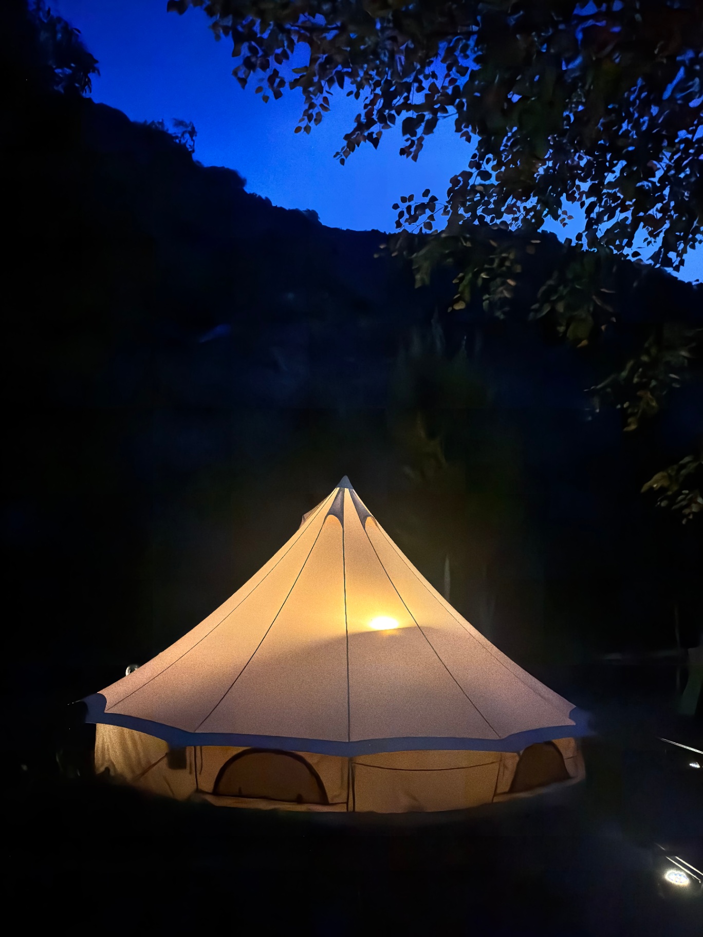 Tienda glamping iluminada con luz cálida de noche junto al río