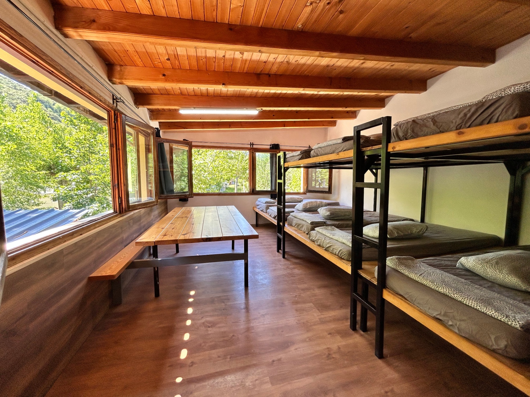 Habitación luminosa del hostel con literas, mesa compartida y ventanas al jardín