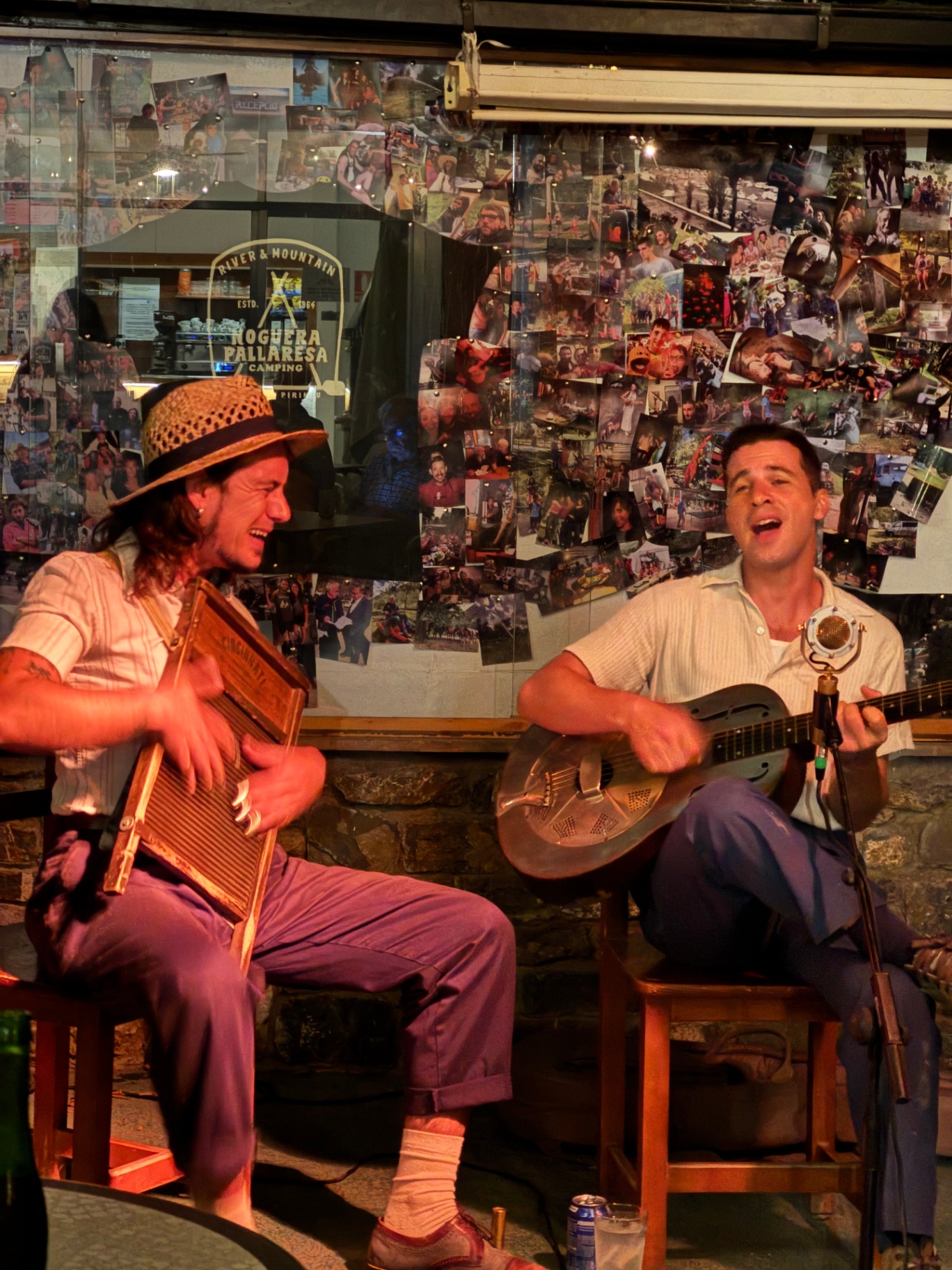 Dos músicos actuando en el interior del camping frente a un mural de fotos